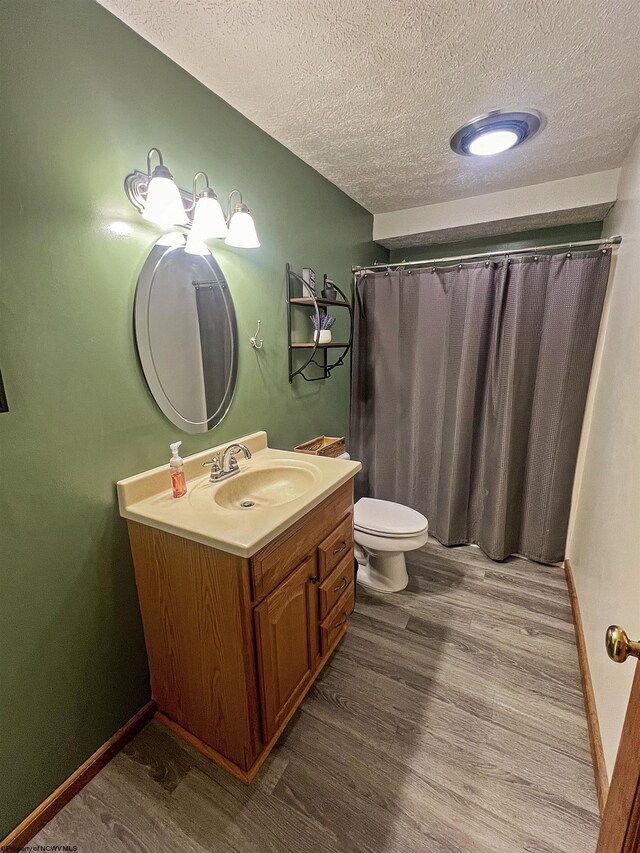 bathroom with a textured ceiling, toilet, baseboards, wood finished floors, and vanity
