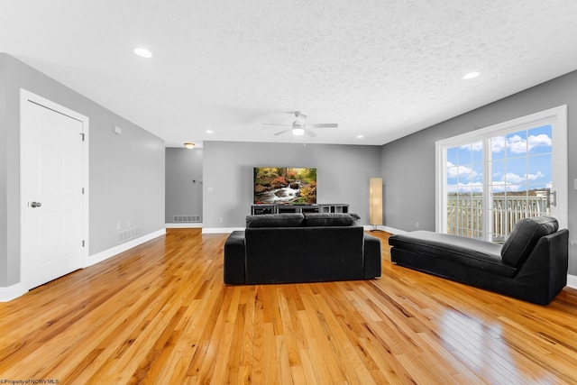 living area with light wood-type flooring, a ceiling fan, visible vents, and a textured ceiling