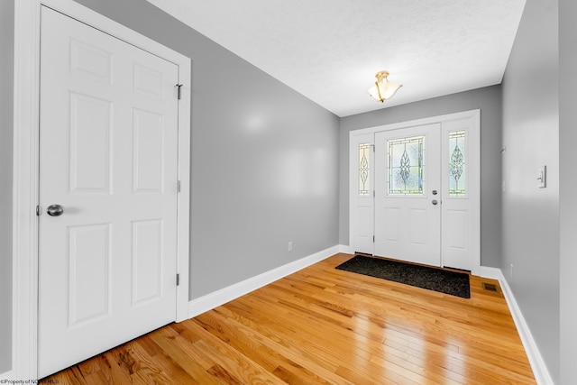 foyer entrance with baseboards, visible vents, and light wood finished floors