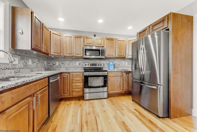 kitchen with light stone counters, a sink, light wood-style floors, tasteful backsplash, and appliances with stainless steel finishes