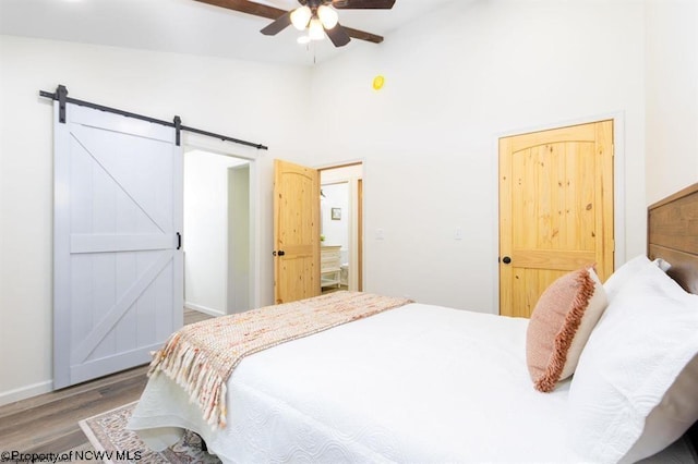 bedroom with wood finished floors, a barn door, baseboards, high vaulted ceiling, and a ceiling fan