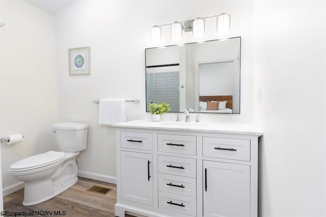 ensuite bathroom featuring vanity, toilet, visible vents, baseboards, and wood finished floors