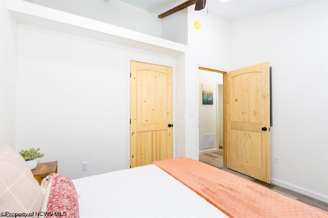 bedroom with beamed ceiling, visible vents, baseboards, wood finished floors, and high vaulted ceiling
