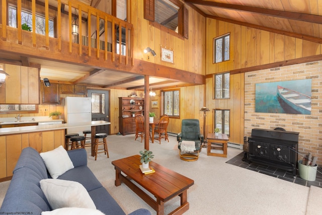 living area with wooden walls, beamed ceiling, and a wood stove
