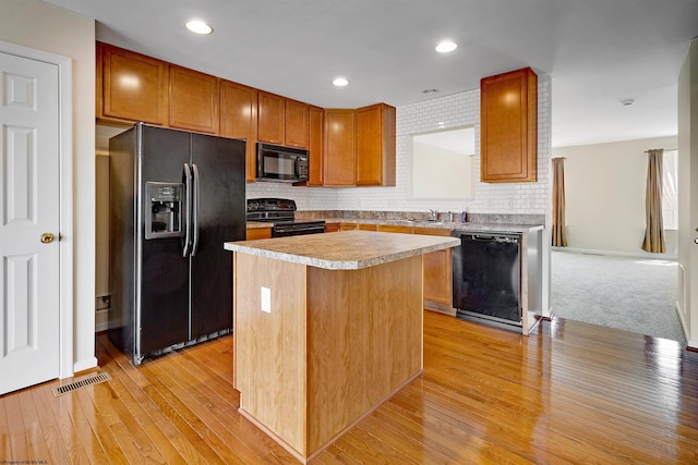 kitchen featuring light wood-style floors, light countertops, a kitchen island, black appliances, and visible vents
