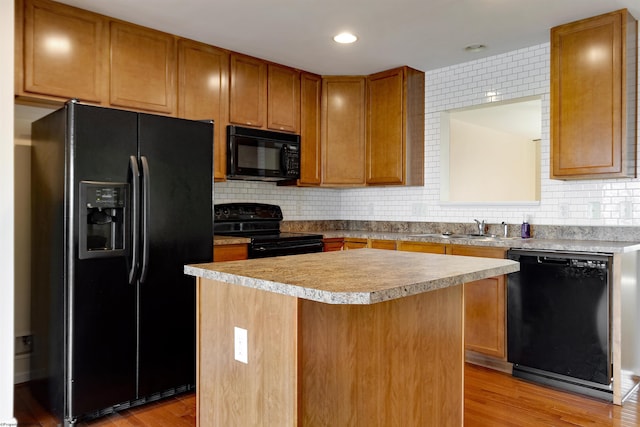 kitchen featuring black appliances, light wood-type flooring, a kitchen island, and backsplash