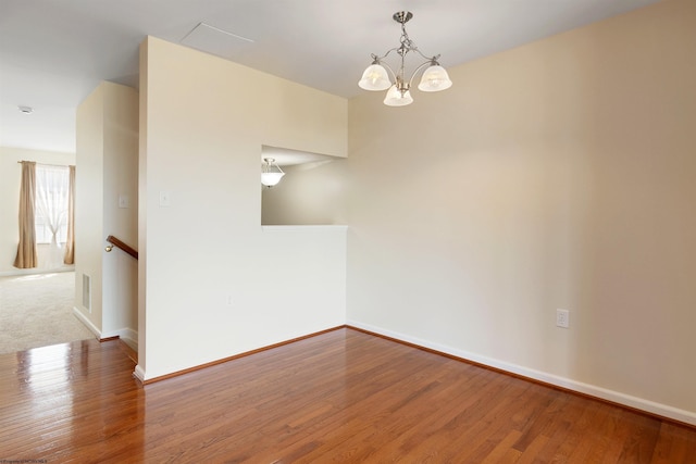 unfurnished room with visible vents, wood finished floors, a notable chandelier, and baseboards
