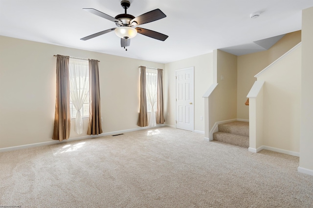 carpeted empty room with baseboards, visible vents, a ceiling fan, and stairway