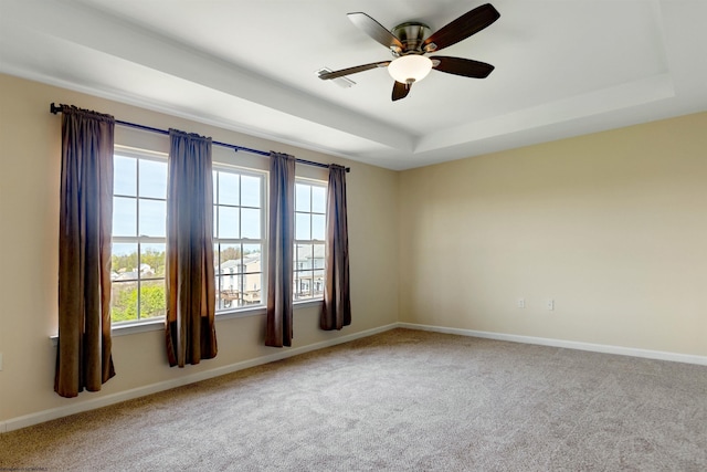 carpeted spare room with baseboards, a ceiling fan, a wealth of natural light, and a tray ceiling