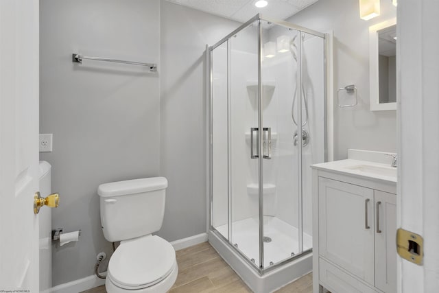 bathroom with vanity, toilet, a stall shower, baseboards, and wood finished floors