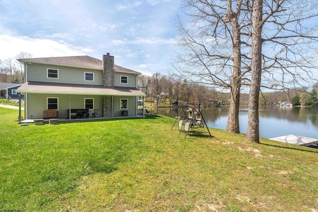 back of house with a patio area, a chimney, a yard, and a water view