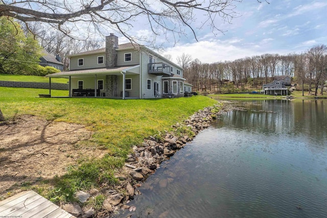 view of side of property with a lawn, a chimney, a water view, and a balcony