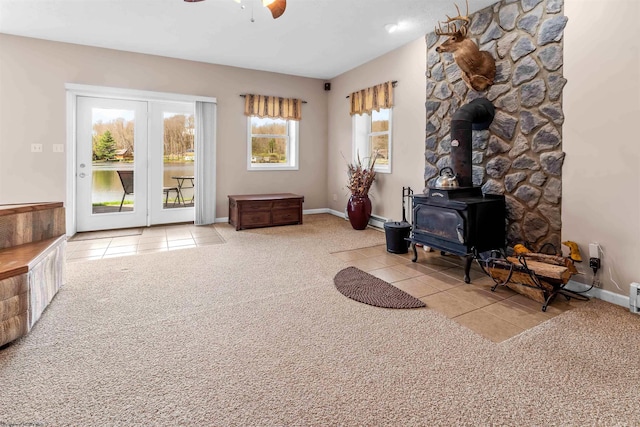 carpeted living room featuring a baseboard radiator, tile patterned floors, ceiling fan, baseboards, and a wood stove