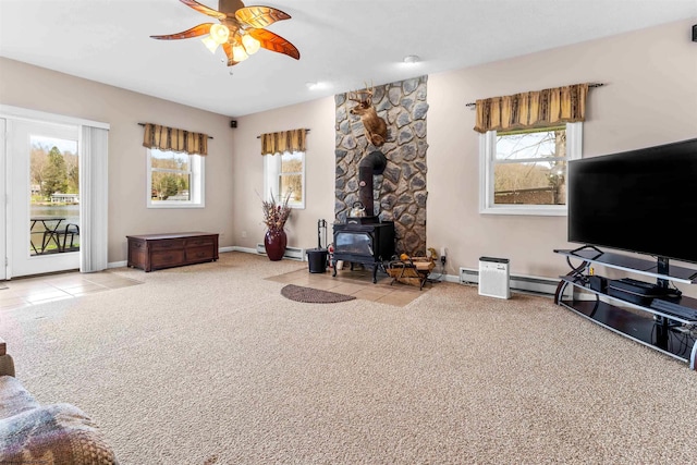 carpeted living area featuring baseboard heating, a wood stove, a ceiling fan, and baseboards