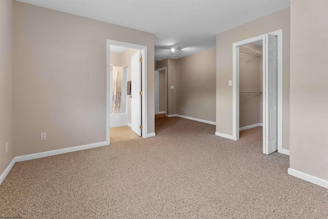 unfurnished bedroom with connected bathroom, a closet, a walk in closet, baseboards, and light colored carpet
