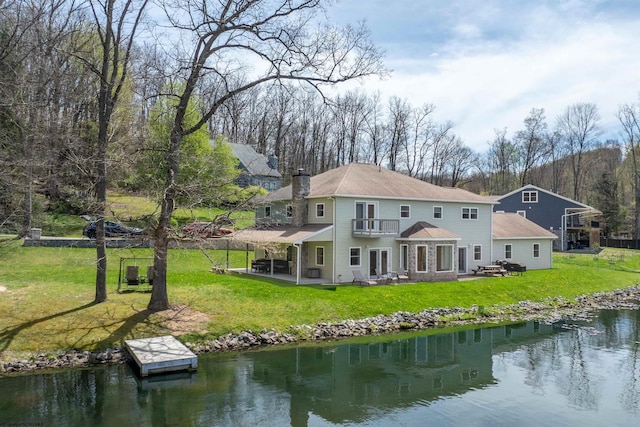 rear view of house with a patio, a balcony, a yard, a water view, and a chimney