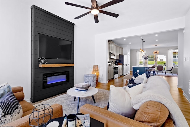 living area featuring a large fireplace, wood finished floors, a ceiling fan, and recessed lighting