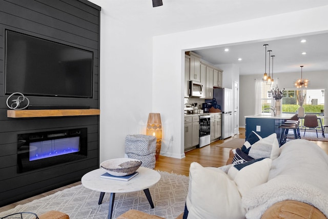 living area featuring baseboards, recessed lighting, light wood finished floors, a fireplace, and a notable chandelier