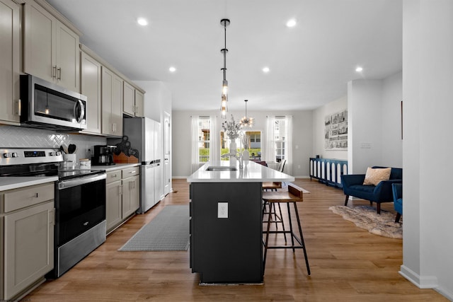 kitchen featuring a sink, stainless steel appliances, a kitchen bar, a center island with sink, and gray cabinetry