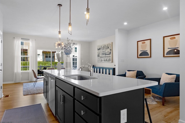 kitchen featuring light wood-style flooring, light countertops, dark cabinetry, a sink, and open floor plan