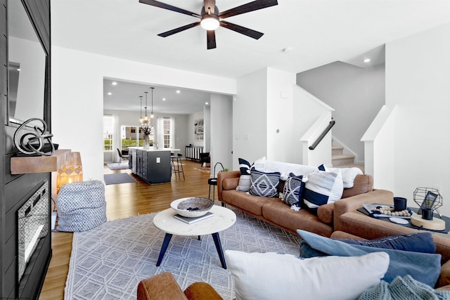 living room with light wood-type flooring, a ceiling fan, recessed lighting, and stairs
