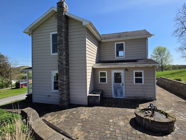 rear view of house with a shingled roof, a patio, and a chimney