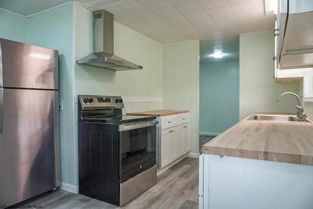 kitchen with wall chimney range hood, appliances with stainless steel finishes, a sink, and light wood finished floors