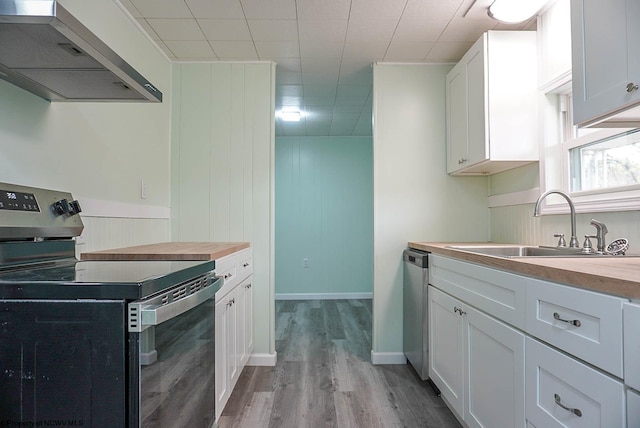 kitchen with butcher block counters, light wood-style floors, wall chimney exhaust hood, a sink, and appliances with stainless steel finishes
