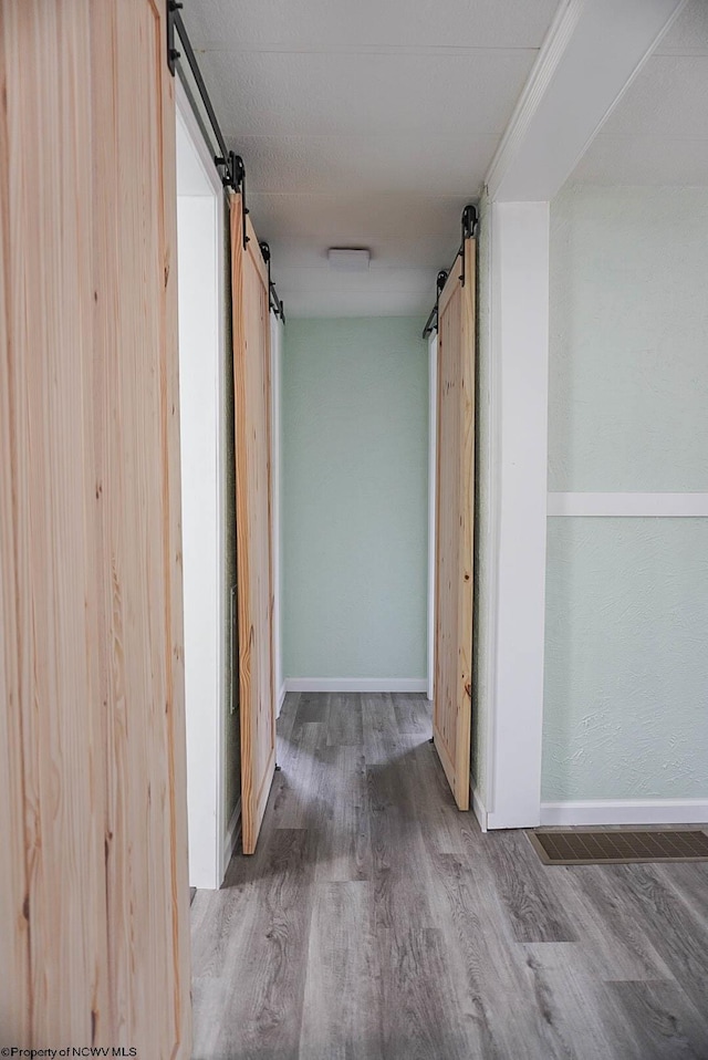 corridor with baseboards, visible vents, a barn door, and wood finished floors
