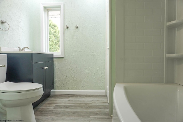 bathroom with wood finished floors, a bathing tub, baseboards, vanity, and a textured wall