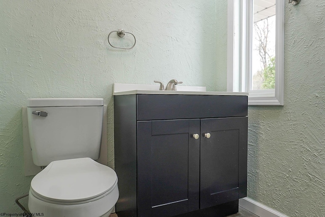 half bath with vanity, a textured wall, baseboards, and toilet