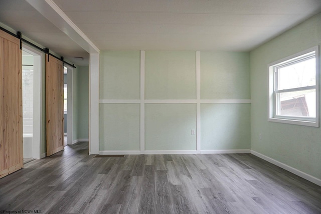 unfurnished room with baseboards, a barn door, and wood finished floors