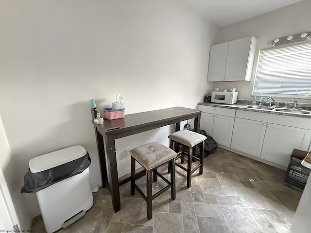 kitchen with a sink, white microwave, and stone tile floors