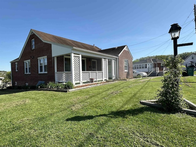 view of side of property with brick siding, a shingled roof, a yard, and covered porch