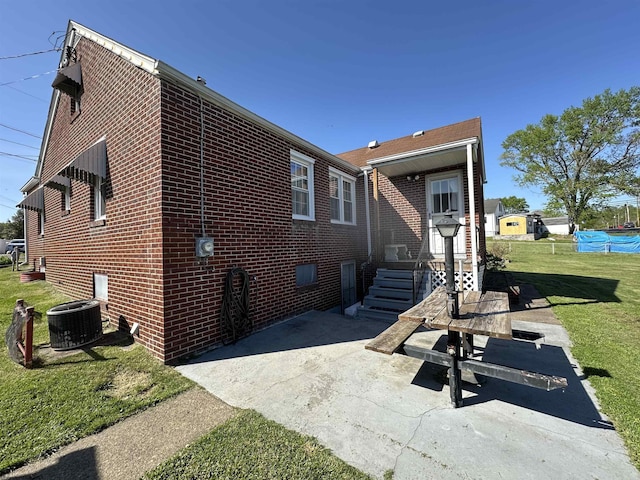 rear view of house with brick siding, a yard, a patio, and cooling unit