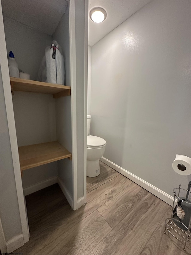 bathroom with toilet, baseboards, and wood finished floors