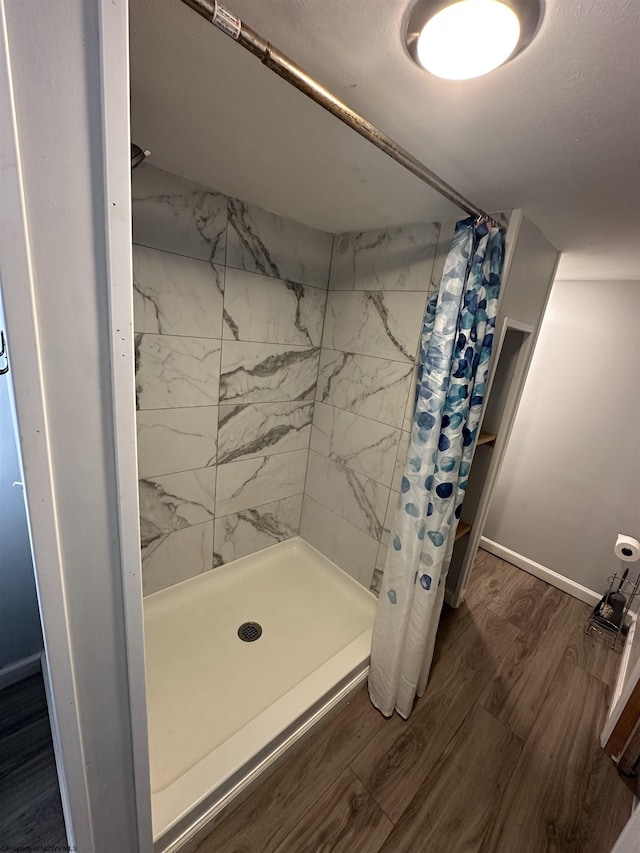 bathroom with baseboards, wood finished floors, and a stall shower