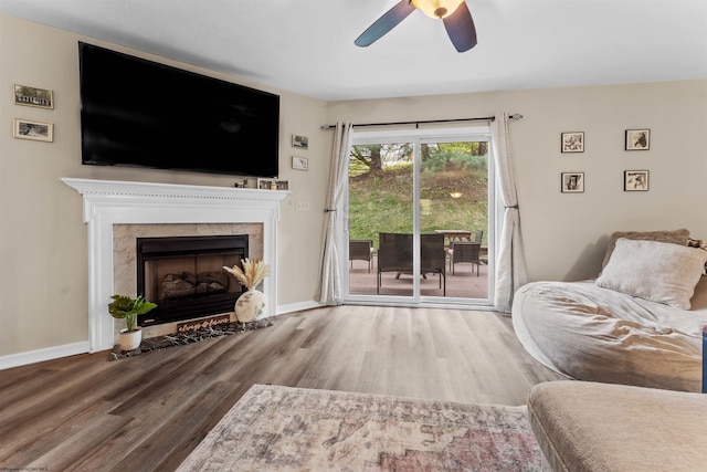 living area featuring baseboards, ceiling fan, wood finished floors, and a fireplace