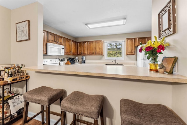 kitchen with brown cabinetry, a breakfast bar area, a sink, a peninsula, and white appliances
