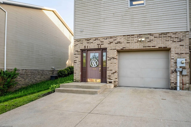 property entrance featuring central air condition unit, brick siding, an attached garage, and driveway