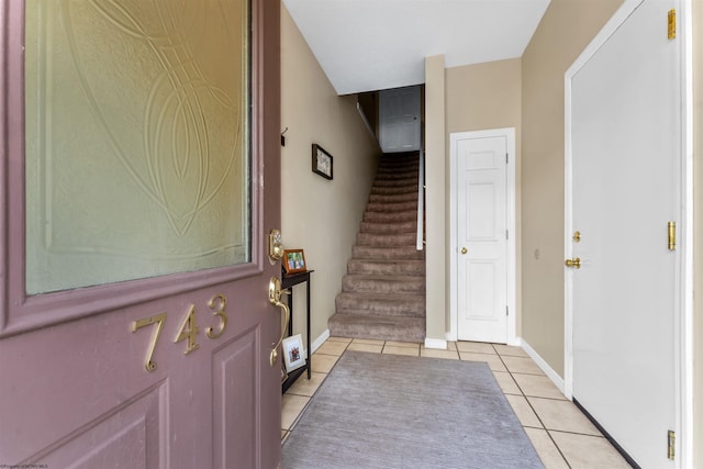 foyer entrance with baseboards, light tile patterned flooring, and stairway