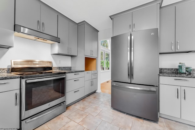 kitchen with under cabinet range hood, dark stone countertops, light tile patterned floors, gray cabinetry, and stainless steel appliances
