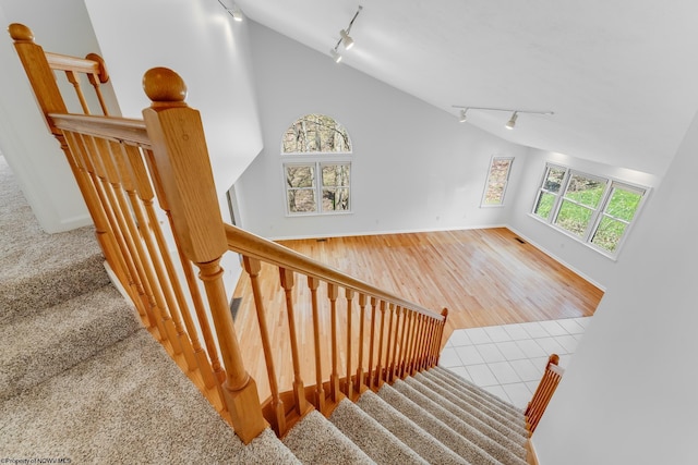 stairs with track lighting, baseboards, and vaulted ceiling