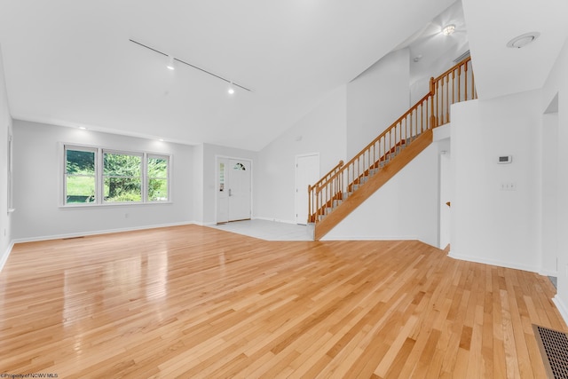 unfurnished living room with track lighting, visible vents, high vaulted ceiling, stairway, and light wood-type flooring