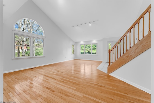 unfurnished living room featuring track lighting, high vaulted ceiling, stairs, baseboards, and hardwood / wood-style flooring