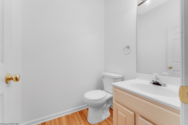 half bathroom with toilet, baseboards, wood finished floors, and vanity