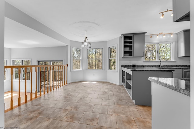 kitchen featuring stainless steel dishwasher, open shelves, a sink, baseboards, and a chandelier