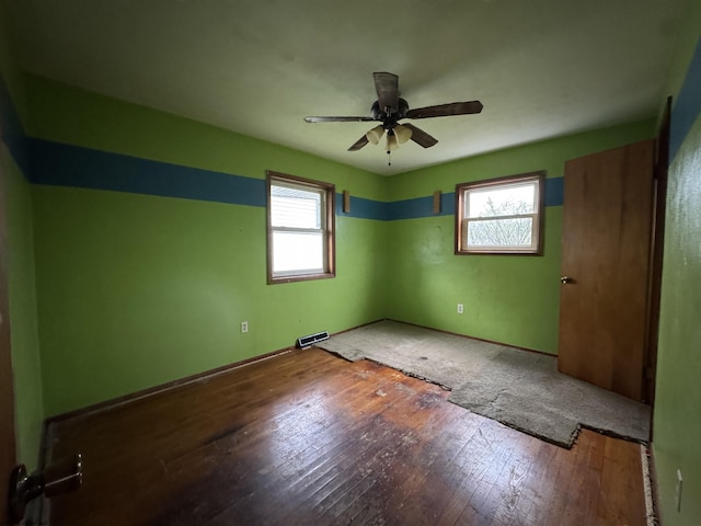 empty room with plenty of natural light, a ceiling fan, visible vents, and hardwood / wood-style flooring