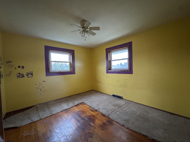 empty room with a healthy amount of sunlight, ceiling fan, wood finished floors, and visible vents
