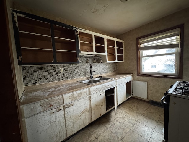 kitchen featuring open shelves, a sink, light countertops, backsplash, and range with gas cooktop